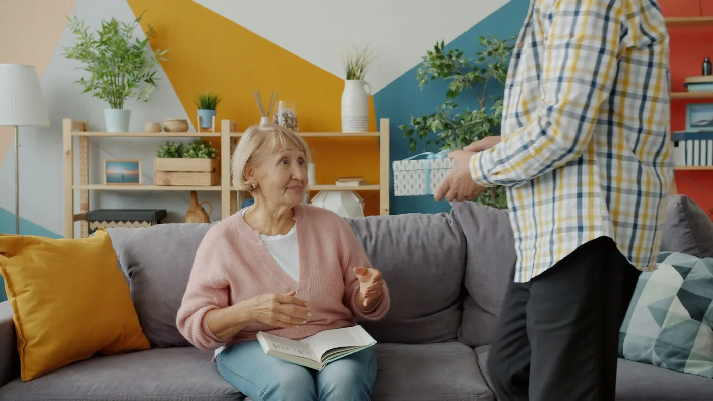 Older woman seated on a sofa beside a standing man